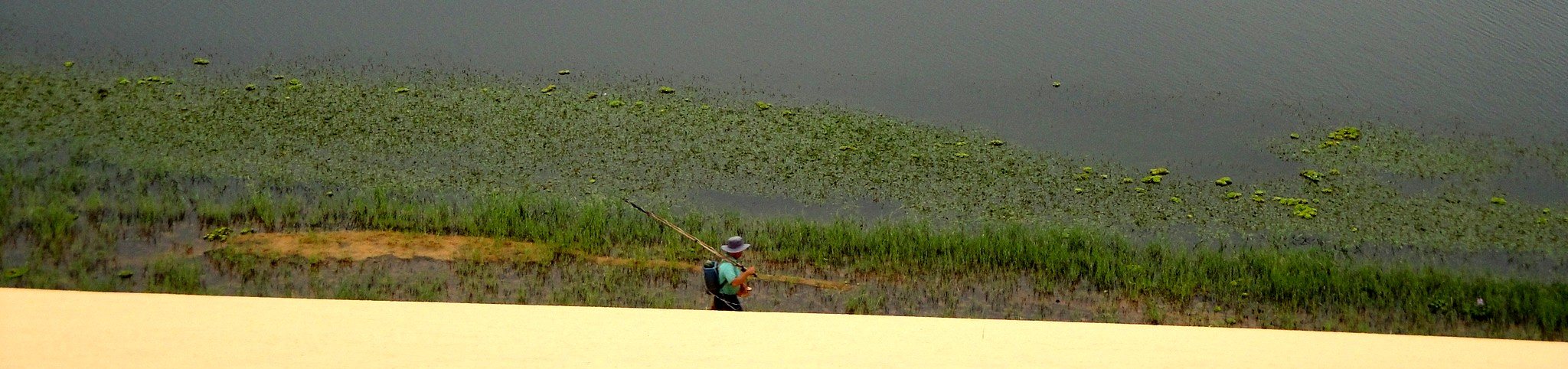 A fisherman on a lakeshore below white sand dunes, Vietnam